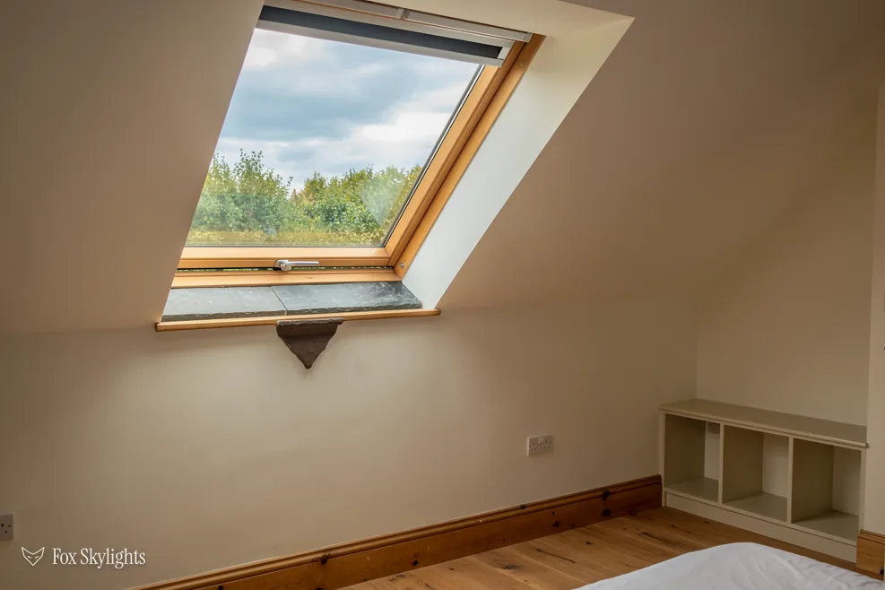Large pine roof window opened wide in a loft bedroom with tree views
