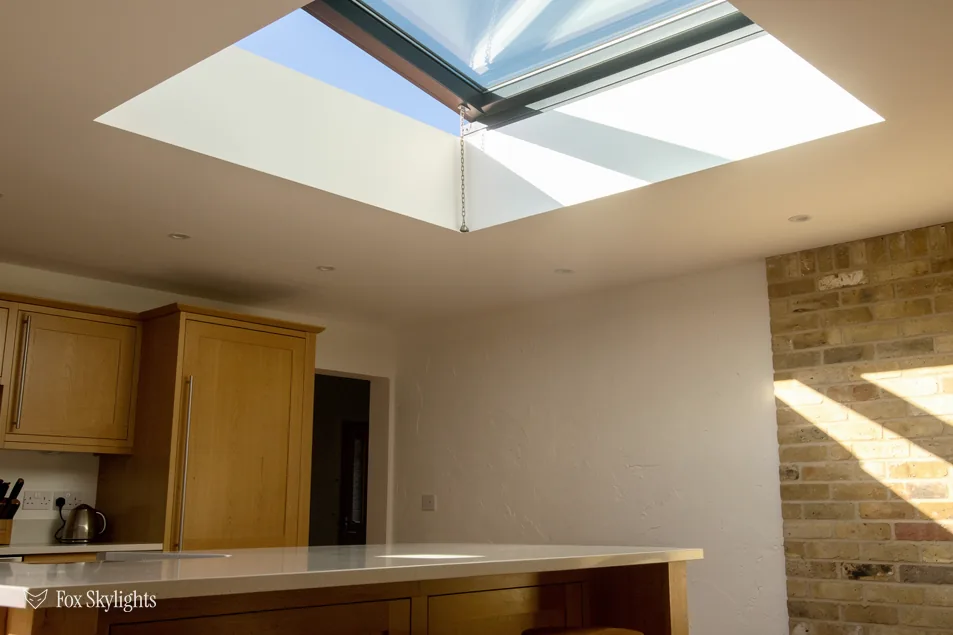 Rooflight casting sunlight onto a kitchen worktop beside a bare brick wall