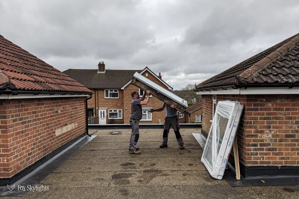 Two fitters carrying a glazed rooflight unit across a flat roof