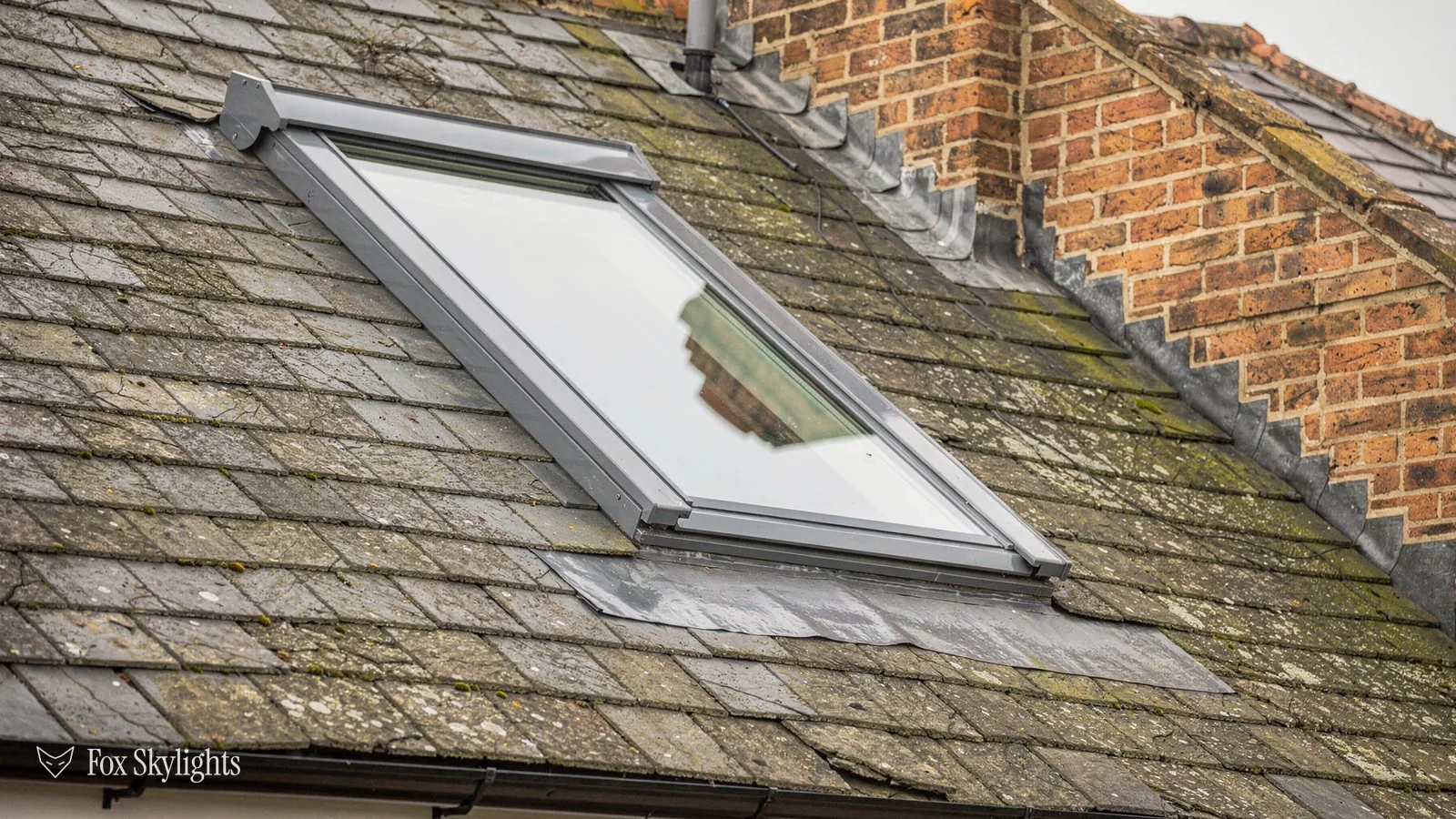 Roof window in a mossy slate roof tight against a brick chimney