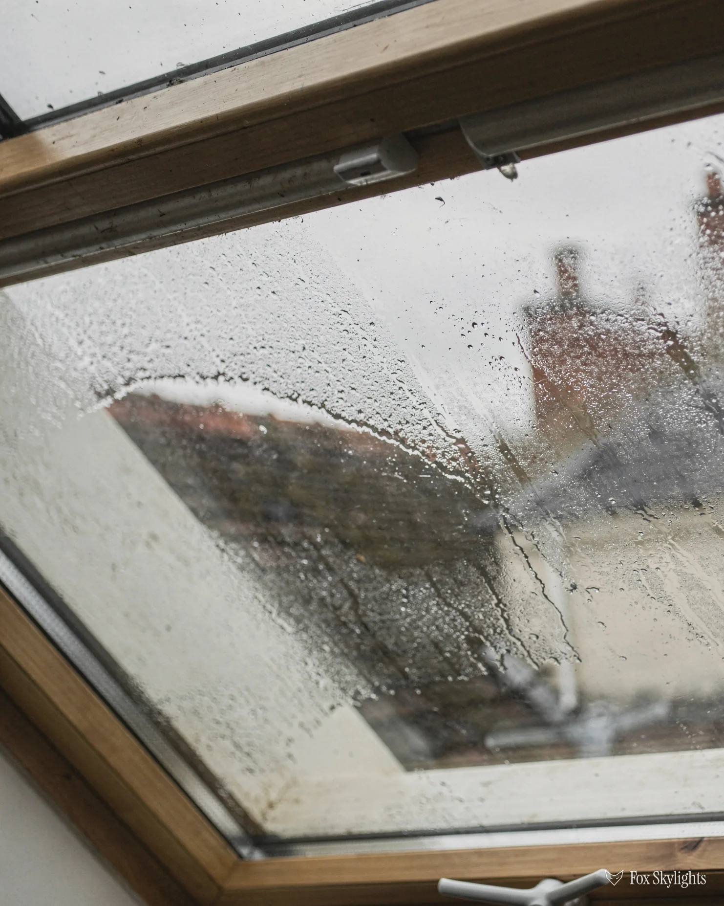 Rain streaked roof window glass with condensation gathering inside the pane