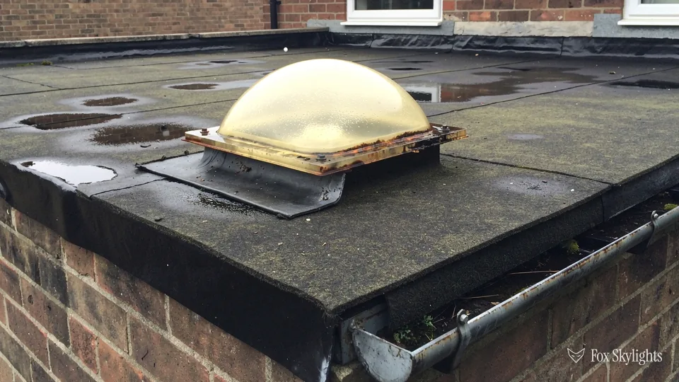 Yellowed plastic dome rooflight on an old flat roof with a brick parapet