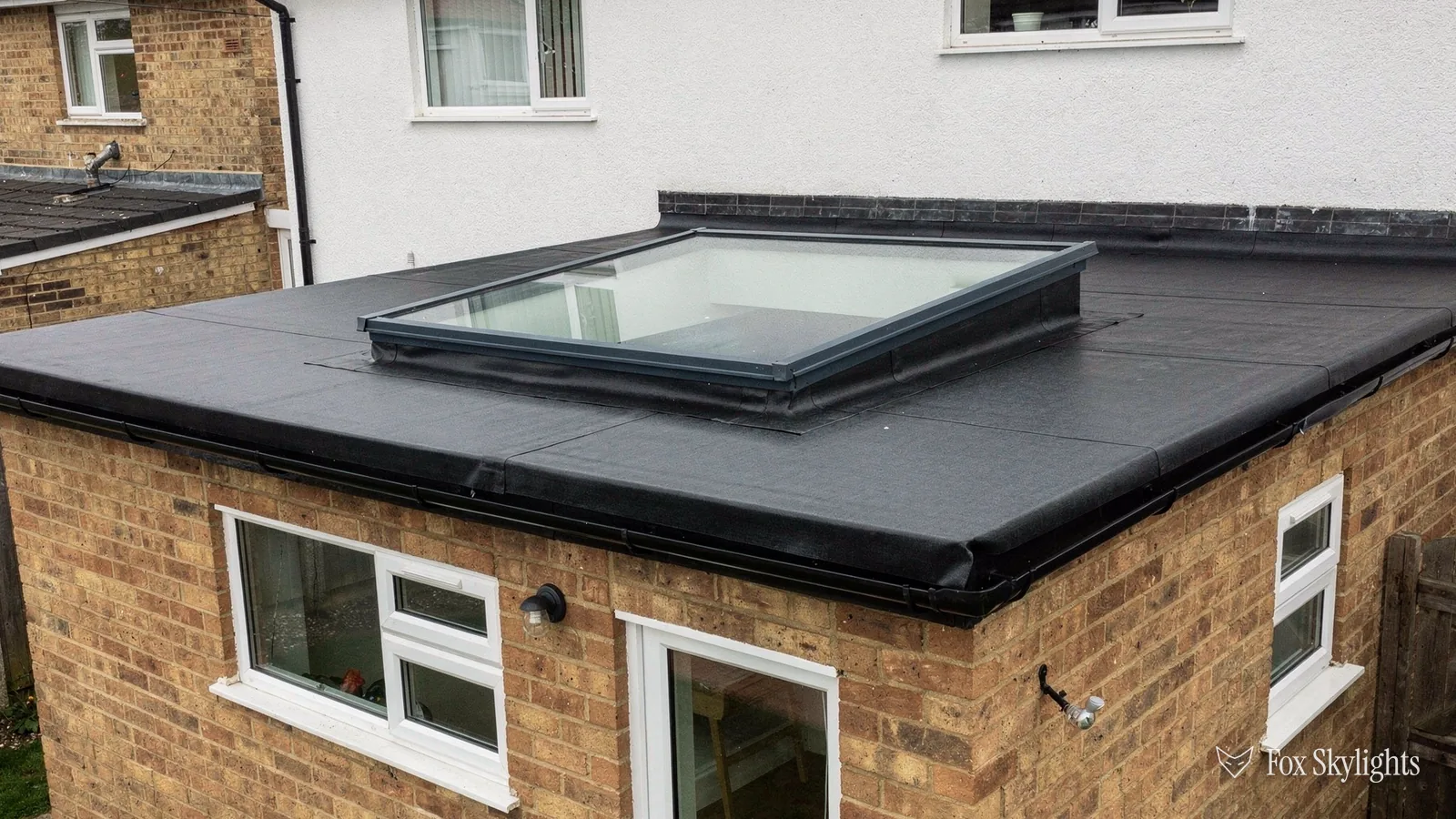 Flat glass rooflight on the black membrane roof of a brick extension