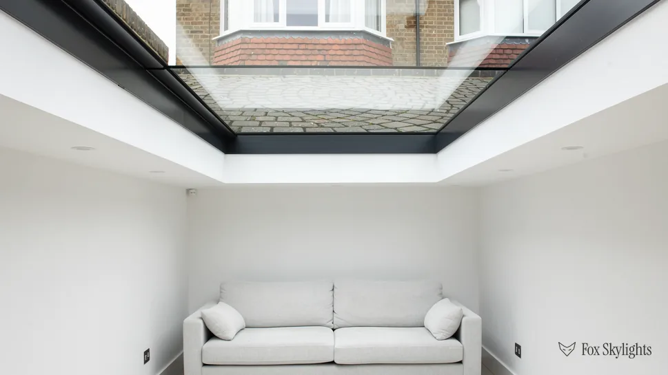 Looking up through a walk on rooflight from a white basement room with sofa