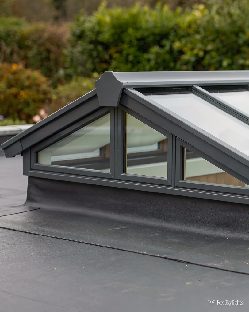 Gabled roof lantern on a grey flat roof with garden shrubs behind