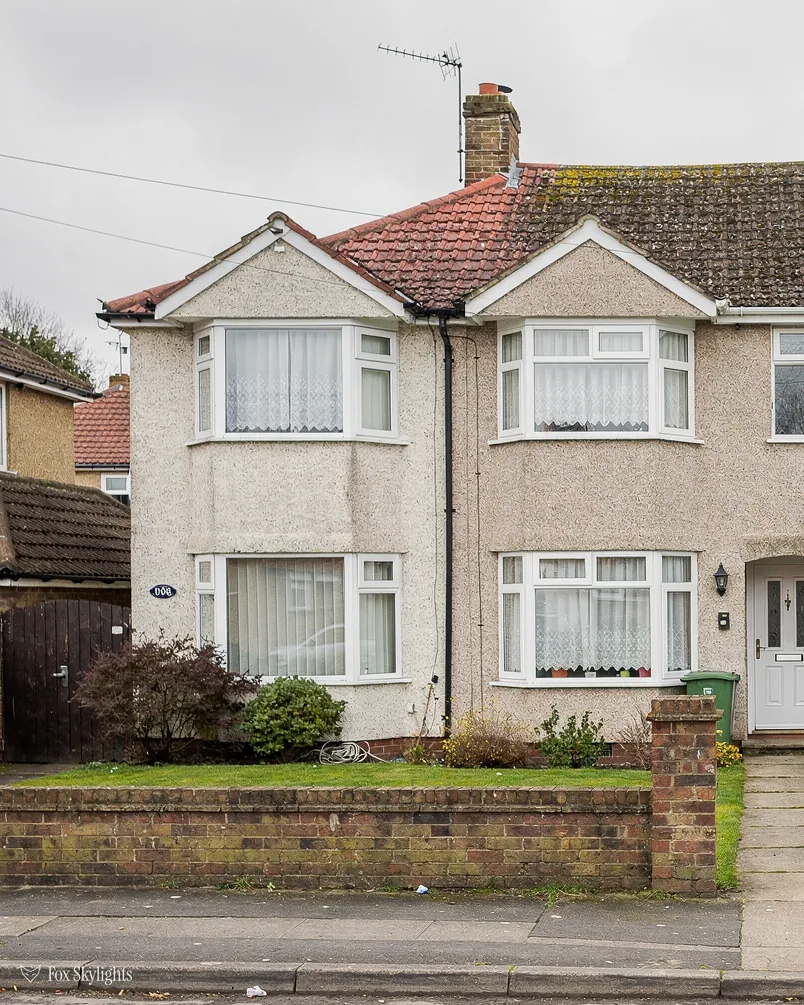 Pebbledash interwar semi with a clay tile roof behind a brick front wall