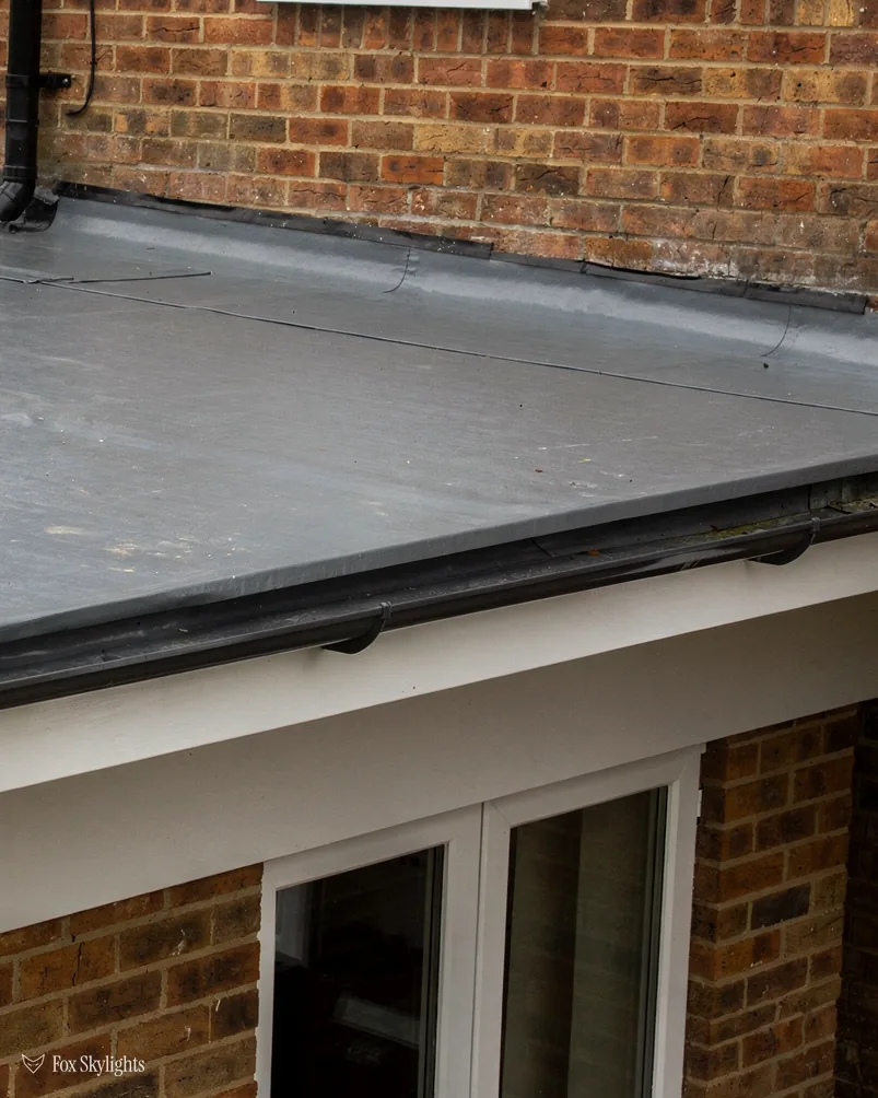 Grey flat roof edge above the French doors of a red brick extension