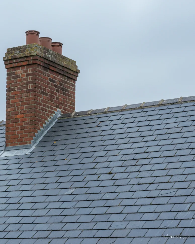 Grey slate roof with a tall red brick chimney stack