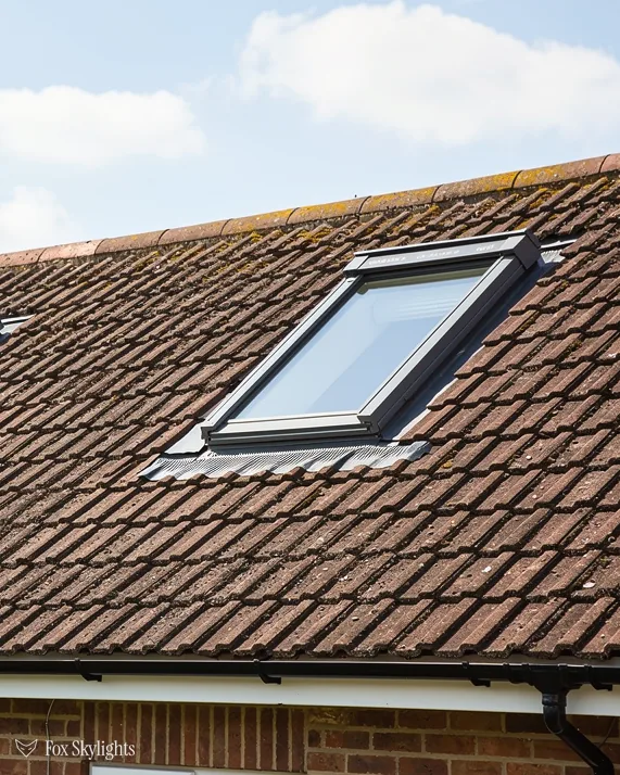 Roof window in a brown concrete tile roof under a bright cloudy sky