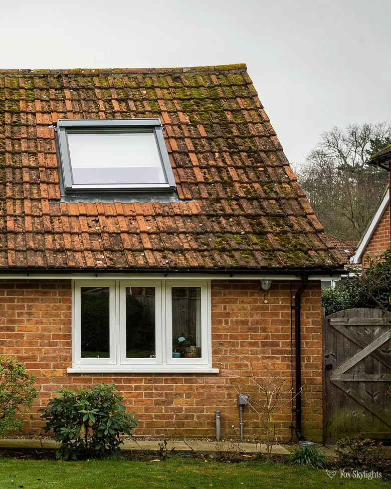 Red brick cottage with a roof window in its mossy clay tile roof