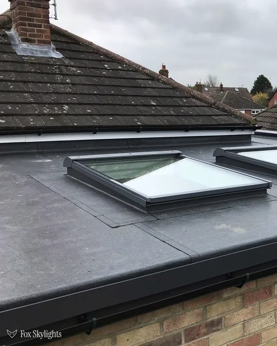 Flat rooflights on a grey membrane extension roof below a tiled house roof