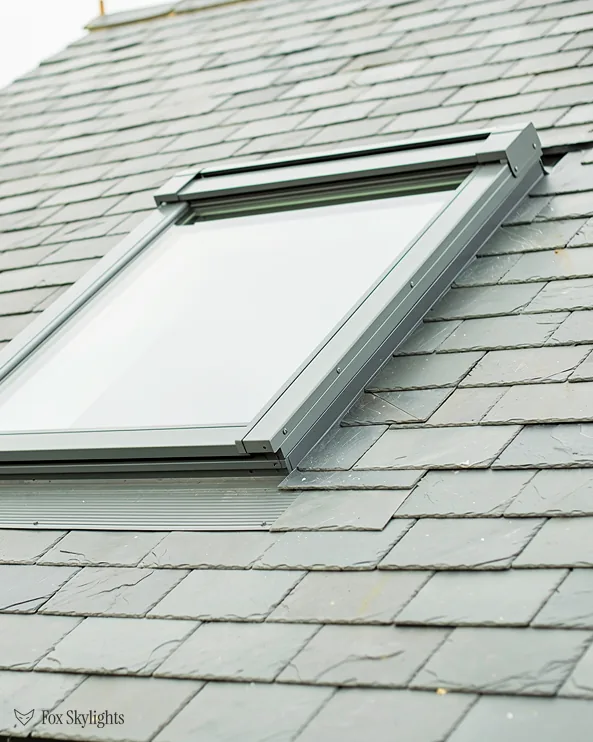 Roof window with grey flashing in a pale slate roof