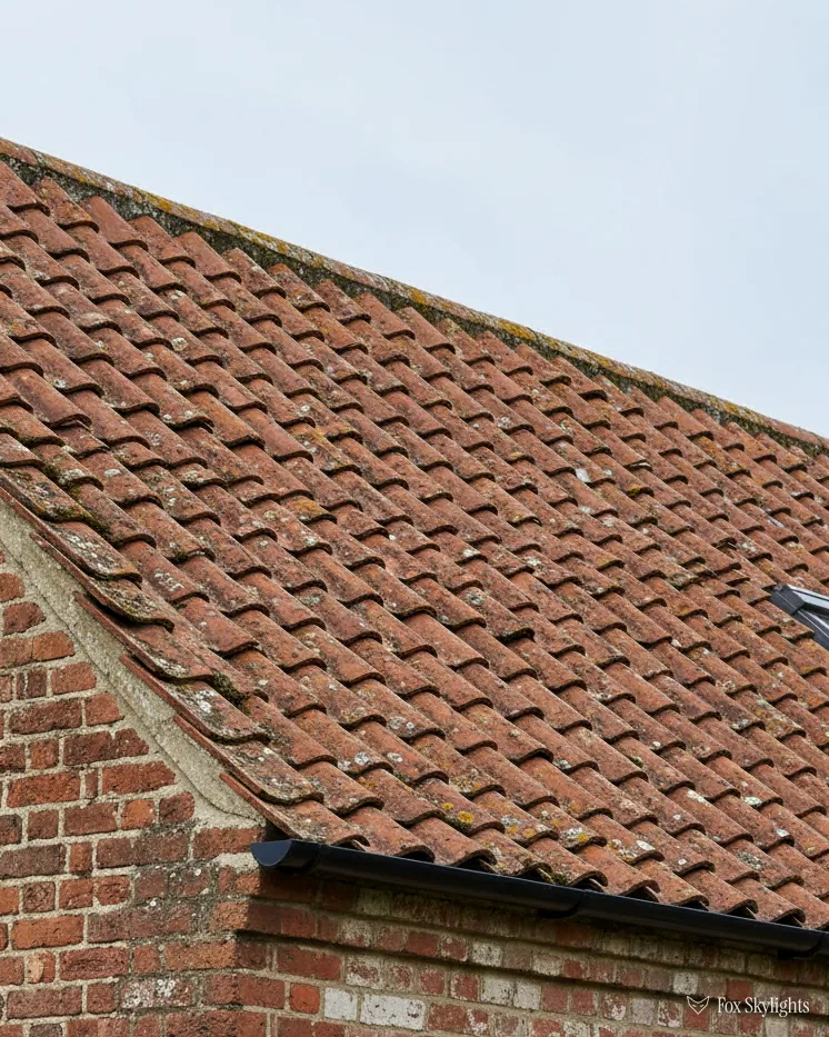 Red clay tile roof over an old brick wall under a pale sky