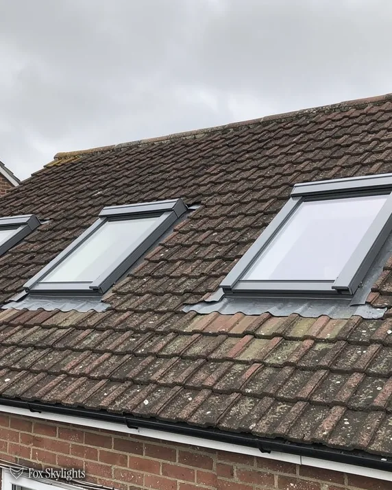 Two roof windows in a brown concrete tile roof above brick walls