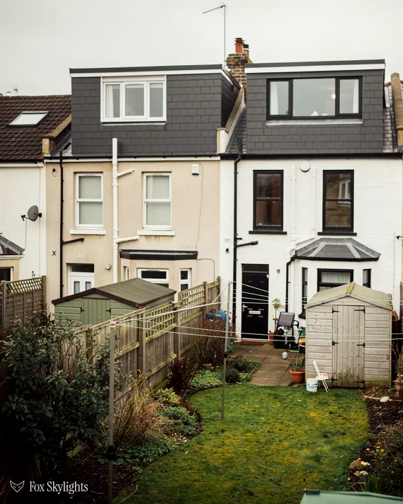 Rear of rendered terraced houses with dark clad dormers and a narrow garden