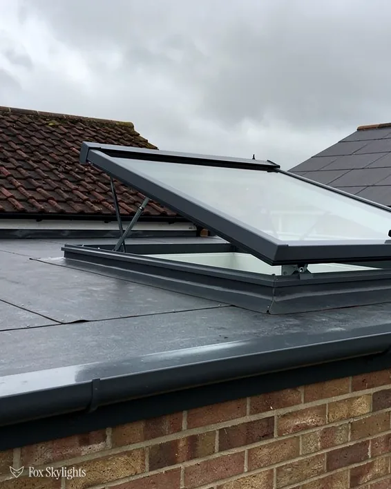 Opening rooflight raised on the flat roof of a brick extension beside tiled roofs