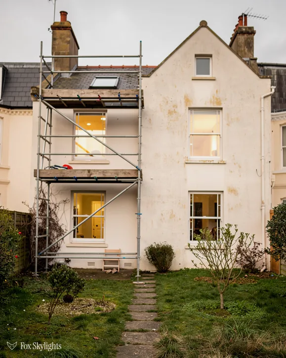 Tall cream rendered period house with scaffold on its rear and a long garden