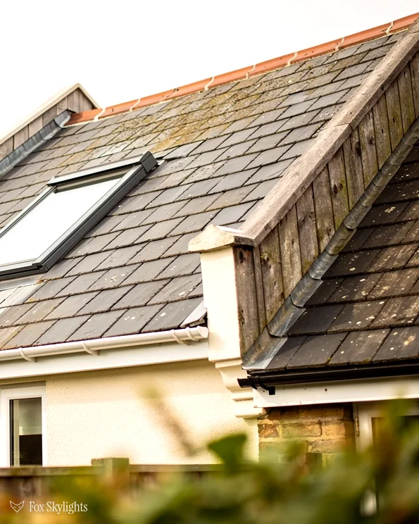 Roof window in the slate roof of a cream rendered house beside a dormer