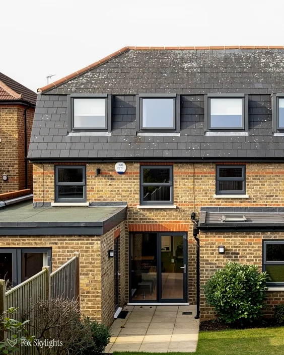 Rear of a yellow brick house with slate roof dormers and a flat roof extension