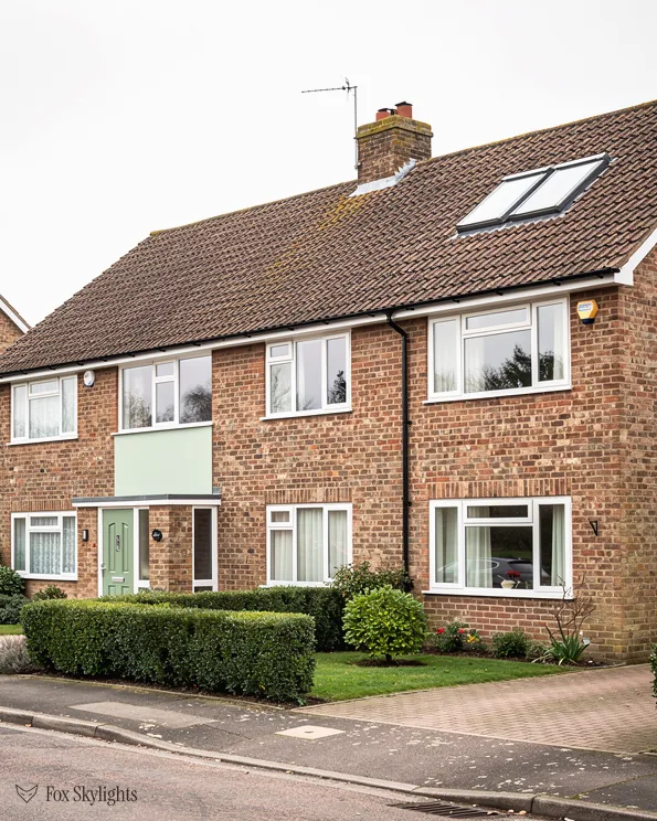 Brick house with a roof window in its clay tile roof and trimmed hedges