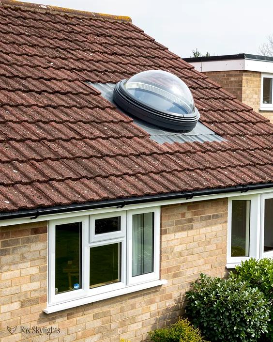 Round dome sun tunnel in a red tile roof above a buff brick house